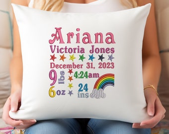 May include: White pillow with rainbow embroidery and the text "Ariana Victoria Jones, December 31, 2023, 9 lbs 6 oz, 4:24 am, 24 ins" in pink and multi-colored thread.