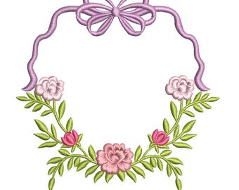 May include: An embroidery design featuring a light purple ribbon frame topped with a bow. The lower section is adorned with light pink roses, smaller dark pink flower buds, and bright green leaves arranged in a symmetrical floral wreath pattern.