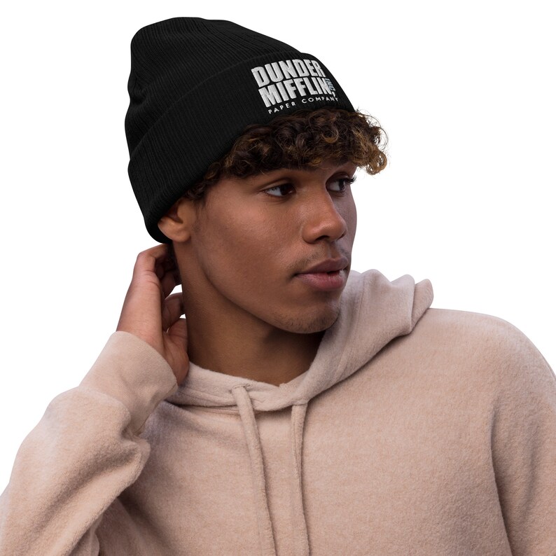 May include: Black knitted beanie with white embroidered text that reads "Dunder Mifflin Paper Company".