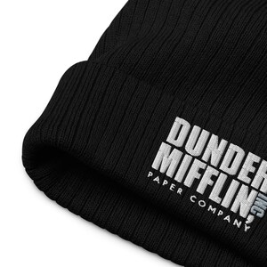 May include: Black knitted beanie with white embroidered text that reads "Dunder Mifflin Paper Company".