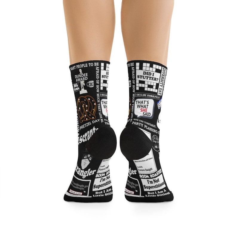 May include: A pair of black socks with a white print featuring quotes and images from the popular television show "The Office". The socks feature a pretzel, the words "That's what she said", and "Diversity Day".