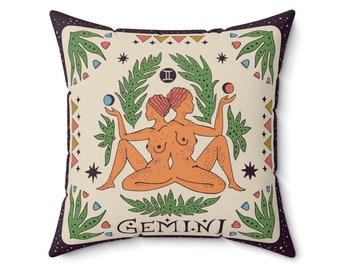May include: A cream-colored throw pillow with a dark purple border features a colorful illustration of the Gemini zodiac sign. The illustration includes two women with orange skin, green leaves, and a yellow, orange, and blue color scheme. The text "GEMINI" is printed in black at the bottom of the pillow.
