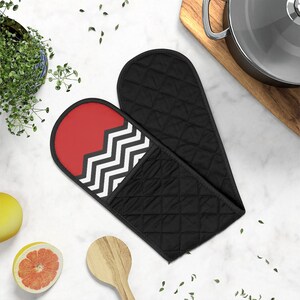 May include: A pair of black quilted oven mitts with a red and black chevron pattern on one mitt. The mitts are on a white marble surface.