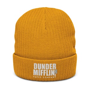 May include: A yellow knitted beanie with the text "Dunder Mifflin Paper Company" embroidered in white.