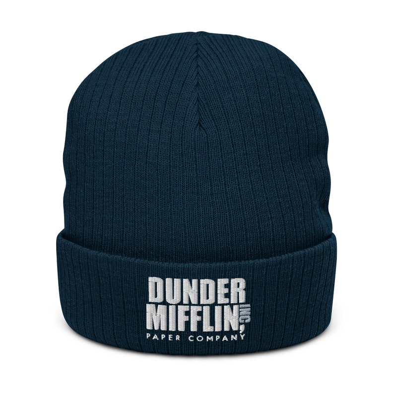 May include: A navy blue knitted beanie with a white embroidered logo that reads "Dunder Mifflin, Inc. Paper Company."