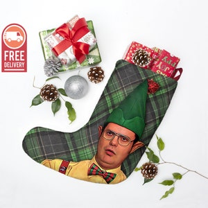 May include: A green and black plaid Christmas stocking with a picture of a man wearing a green elf hat and glasses. The man is wearing a yellow shirt with a red bow tie. The stocking has a white trim and a red and white ribbon.