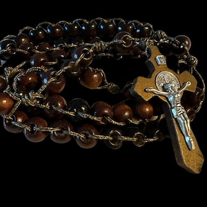 May include: A brown wooden rosary with a brown wooden crucifix featuring a silver figure of Jesus Christ. The crucifix has the inscription "IN RI" on the top.