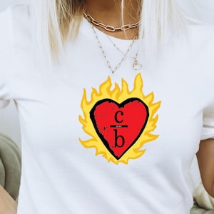 Pode incluir: Camiseta branca com um gráfico de coração vermelho em chamas. O coração tem as letras "C" sobre "b" dentro.
