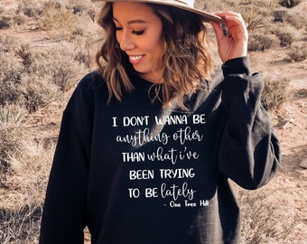 Op de afbeelding: Een zwart sweatshirt met witte tekst die luidt: "Ik wil niets anders zijn dan wat ik de laatste tijd probeer te zijn - One Tree Hill".