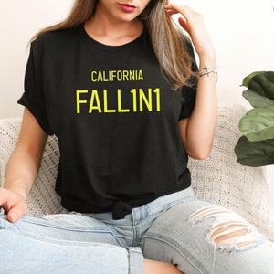 Op de afbeelding: Een zwart T-shirt met de tekst "CALIFORNIA FALL1N1" in gele letters.