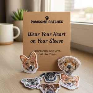 May include: A collection of six embroidered dog face patches arranged in front of a tan cardboard display card. The card features the text PAWSOME PATCHES, Wear Your Heart on Your Sleeve, and Embrdonded with Love, Just Like Them in black ink.