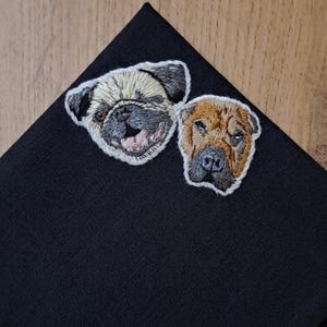 Black pocket square with an embroidered pug face and a brown wrinkle-faced dog, showing how a pet portrait stands out on dark fabric.