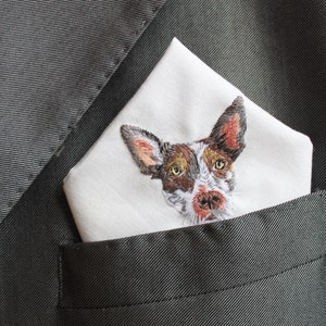 Angled view of a custom embroidered pet handkerchief in a groom's dark suit pocket, showing the thread texture of the dog's face and ears.