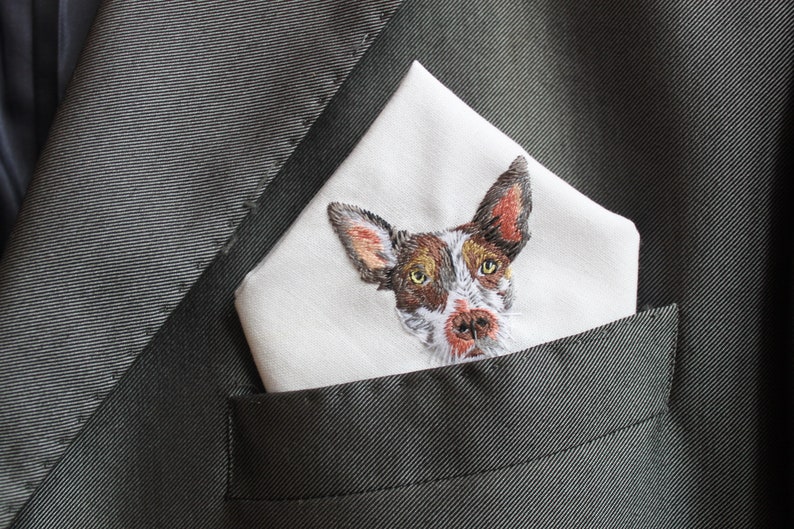 Angled view of a custom embroidered pet handkerchief in a groom's dark suit pocket, showing the thread texture of the dog's face and ears.