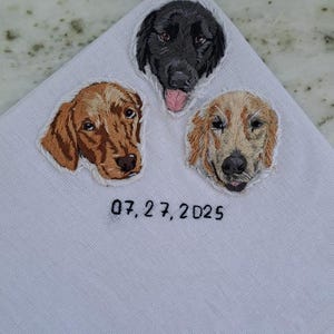 White pocket square with three embroidered dog portraits (a black Lab, a red retriever and a golden retriever) and a wedding date stitched underneath.