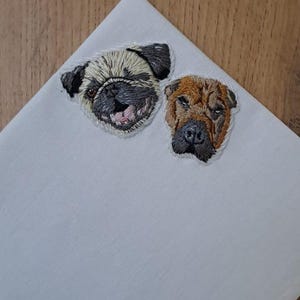 Light gray pocket square with embroidered portraits of a fawn pug and a brown wrinkle-faced dog side by side.