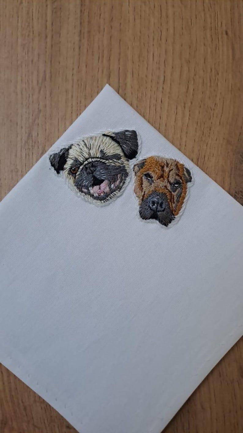 Light gray pocket square with embroidered portraits of a fawn pug and a brown wrinkle-faced dog side by side.