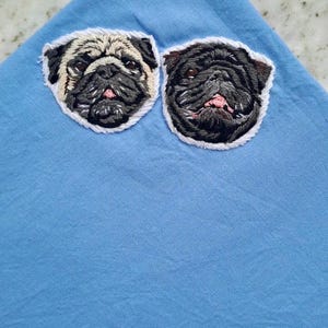 Light blue pocket square embroidered with two pug faces, one fawn and one black, an example of a two-pet portrait.