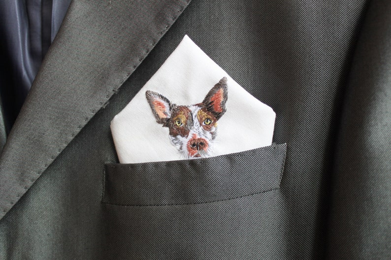 Personalized dog pocket square folded in a gray suit jacket pocket, with the embroidered pet portrait showing just above the pocket line.