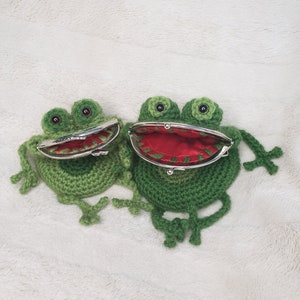 Può includere: Due portafogli a forma di rana in crochet verde con occhi neri e bocche rosse. Un portafoglio è aperto, rivelando una fodera rossa.