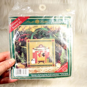 May include: A Mill Hill Buttoned & Beaded Kit titled The Stockings Were Hung, featuring a cross-stitch pattern of a fireplace with stockings, a cat, and gifts. The package includes glass beads, ceramic buttons, perforated paper, floss, needles, and ribbon.