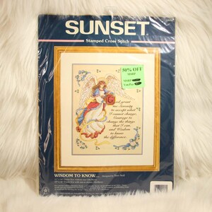 Op de afbeelding: Een Sunset stempelkruissteekkit met een engelontwerp en de tekst "God grant me Serenity..." Het ingelijste kunstwerk heeft een gouden rand en is verpakt in een blauwe en transparante plastic hoes. De kit is gemarkeerd met 50% korting.