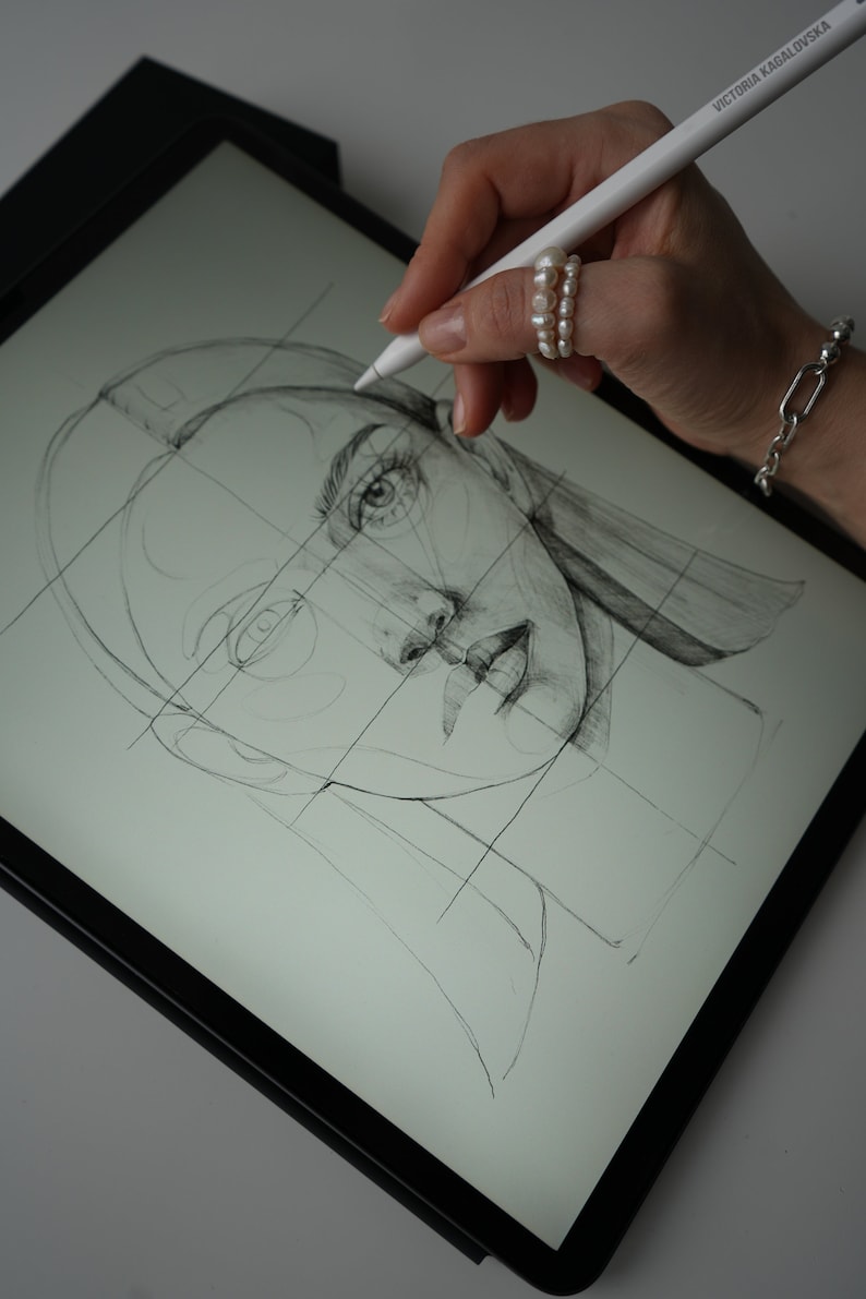 May include: A hand uses a stylus to draw a portrait of a woman on a digital drawing tablet. The woman's face is drawn in pencil and is divided into sections by a grid.