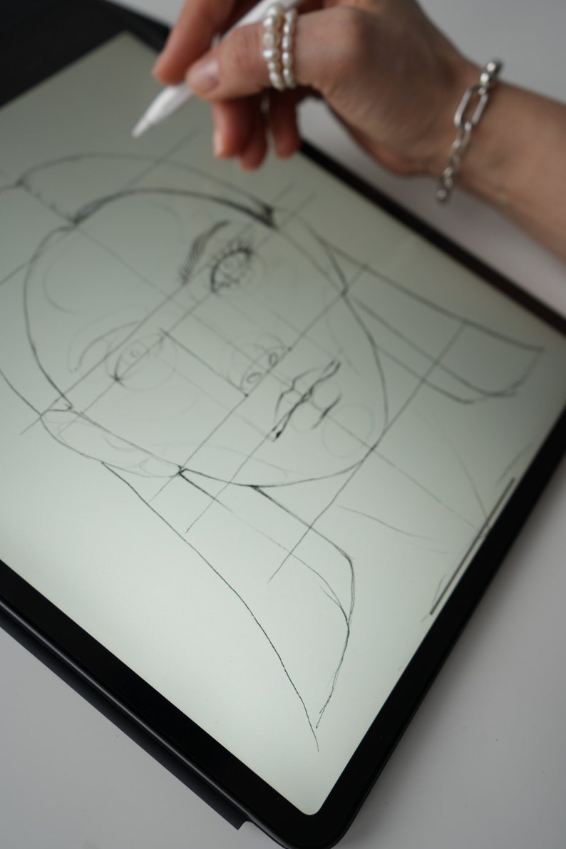 May include: A close-up of a digital drawing of a face on a tablet screen. The face is drawn with a grid overlay, and the artist is using a stylus to draw the details.