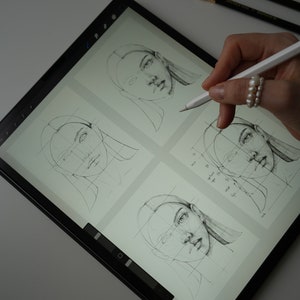 May include: A digital drawing tablet with a stylus pen, showing four different sketches of a woman's face. The sketches are drawn on a grid, and the stylus pen is being used to draw on the tablet.