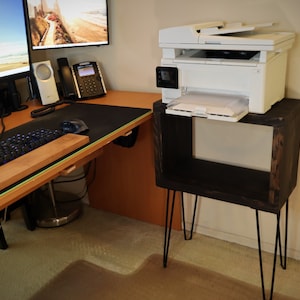 May include: A white printer sits on a dark wood shelf with black hairpin legs. The shelf is next to a desk with a keyboard and mouse.