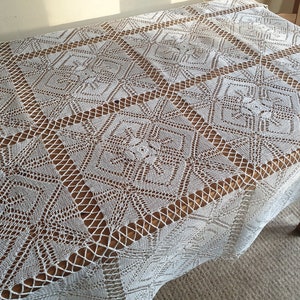 May include: White crocheted tablecloth with a geometric pattern. The tablecloth is laid on a wooden table.