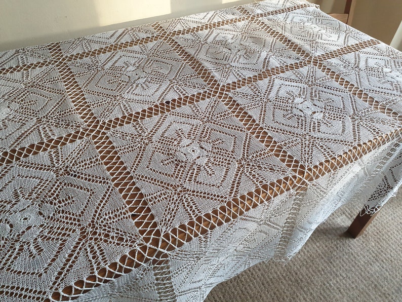 May include: White crocheted tablecloth with a geometric pattern. The tablecloth is laid on a wooden table.