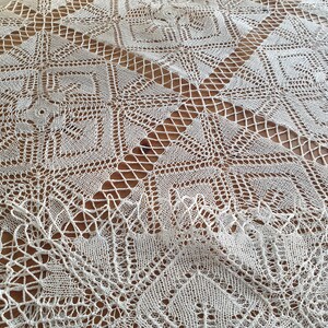 May include: White crocheted tablecloth with a delicate, intricate pattern. The tablecloth is laid out on a wooden surface.