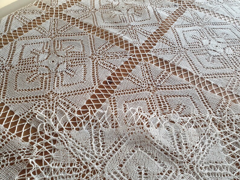 May include: White crocheted tablecloth with a delicate, intricate pattern. The tablecloth is laid out on a wooden surface.