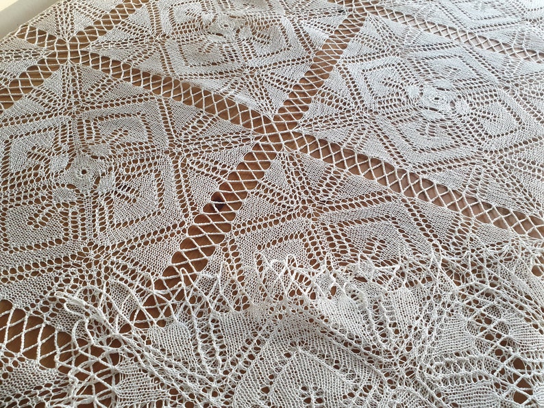 May include: White crocheted tablecloth with a geometric pattern. The tablecloth has a delicate, lacy design with a square shape.