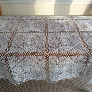 May include: White crocheted tablecloth with a geometric pattern. The tablecloth is laid out on a wooden table.