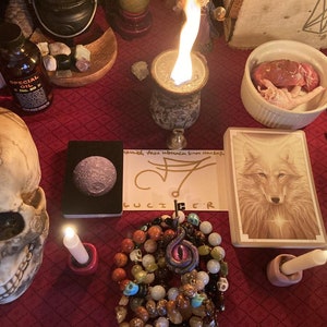 May include: A red table with a skull, candles, a bowl with raw meat, a tarot card with a wolf, a bracelet with an eye charm, and a bottle of special oil.