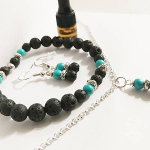 Op de afbeelding: Een sieradenset met een armband, oorbellen en een ketting. De set bevat zwarte lavasteenkralen, turquoise kralen en zilverkleurige accenten. De ketting heeft een hanger met een turquoise kraal en een lavasteenkraal.