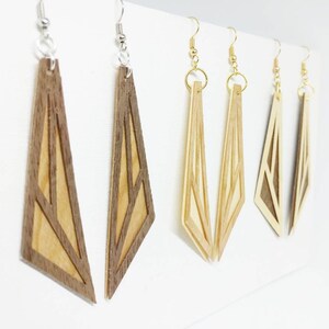 Puede incluir: Un conjunto de cuatro pendientes de madera con diseños geométricos. Los pendientes están hechos de dos capas de madera, con la capa superior recortada para crear un patrón geométrico. Los pendientes están disponibles en dos combinaciones de colores: marrón y madera natural, y madera natural con un acento marrón claro.