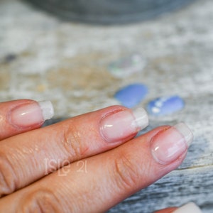 May include: Close-up of a hand with several fingernails that have been recently manicured with a clear gel polish and a white tip.