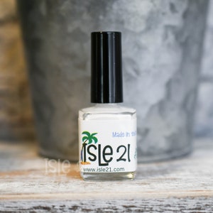 May include: A white bottle of nail polish with a black cap. The bottle has a label with a palm tree and the text "Isle 21" and "www.isle21.com". The label also says "Made in the USA".