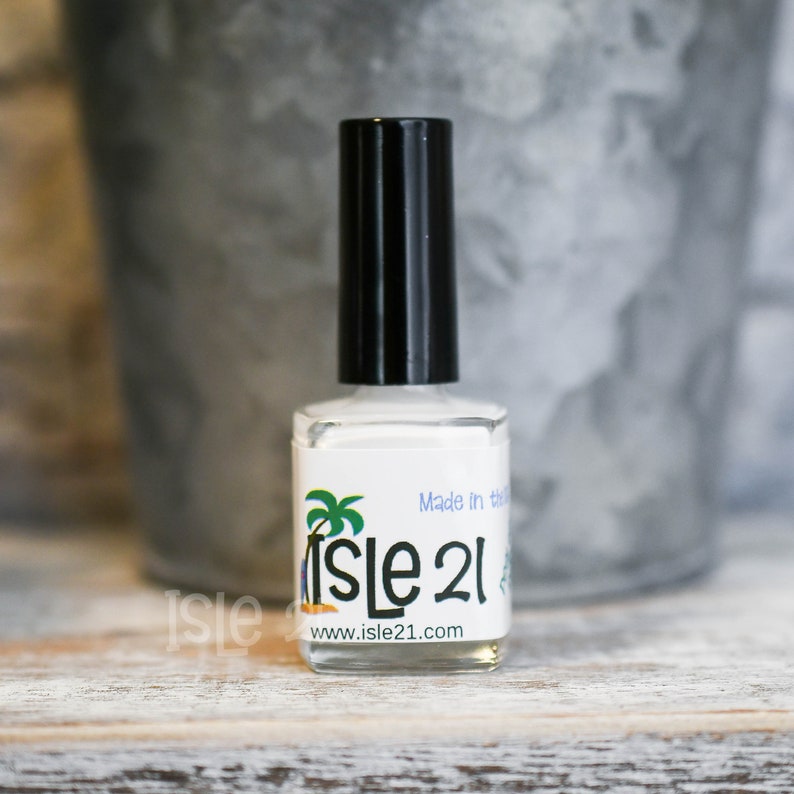 May include: A white bottle of nail polish with a black cap. The bottle has a label with a palm tree and the text "Isle 21" and "www.isle21.com". The label also says "Made in the USA".