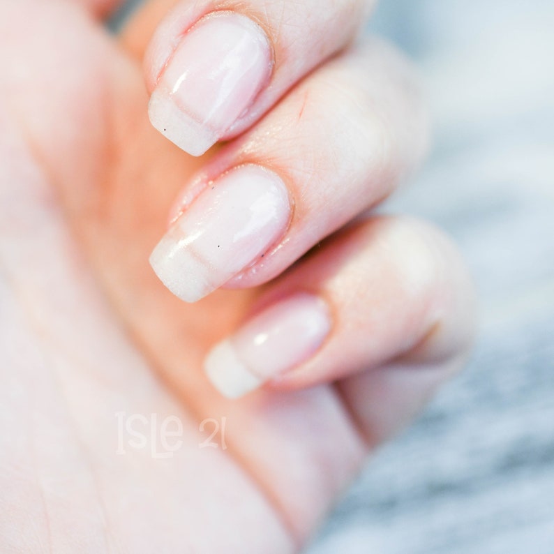 May include: Close-up of a hand with four fingernails painted with a sheer, milky white nail polish.