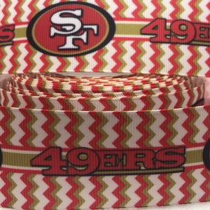 以下が含まれることがあります： サンフランシスコ・フォーティナイナーズのロゴと「49ers」の文字が入った、赤、白、金のヘリンボーン柄のリボンです。