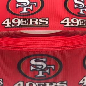 以下が含まれることがあります： サンフランシスコ・フォーティナイナーズのロゴと「49ers」の文字が印刷された赤と金のリボンです。