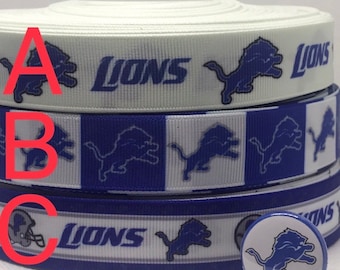 May include: Three rolls of white and blue ribbon with the Detroit Lions logo. The ribbon is available in 7/8" and 1.5" widths. A small blue and white button with the Lions logo is also shown.