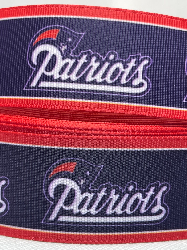 May include: Red, white, and blue ribbon with the word "Patriots" printed in white on a navy blue background.