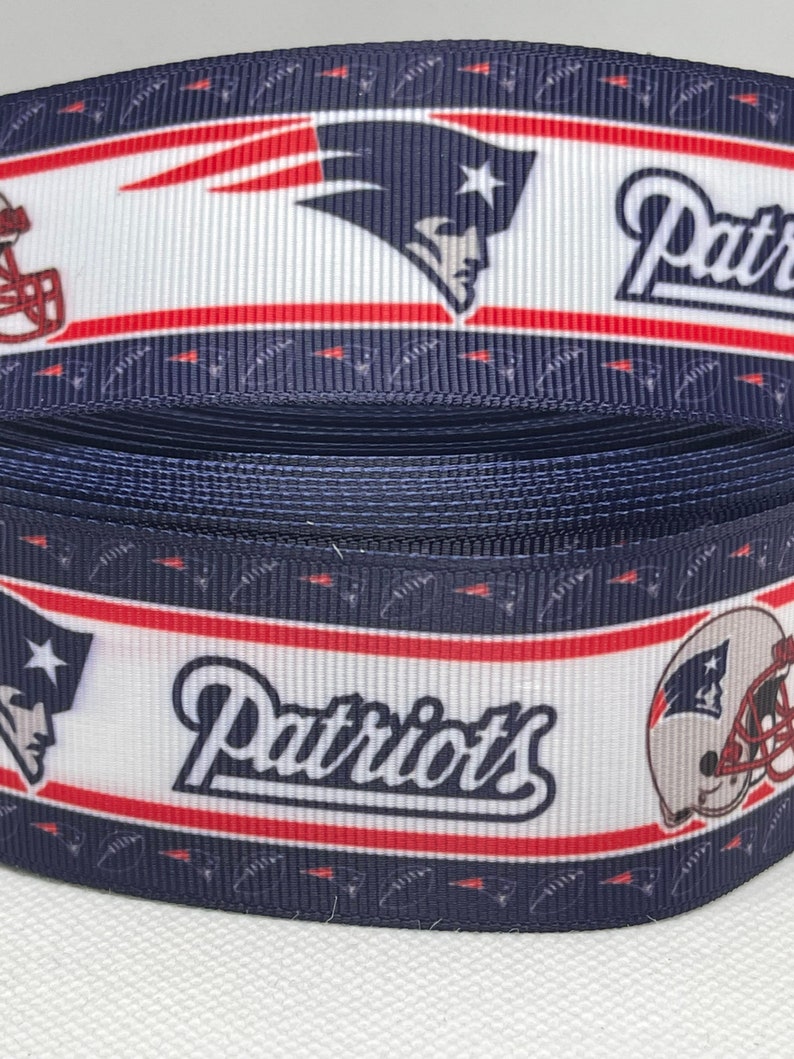 May include: A blue, white, and red ribbon with the New England Patriots logo and the word "Patriots" printed on it.