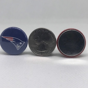May include: Three round buttons, one with a blue background and a white and red logo of a football team, one with a silver US quarter with the text "UNITED STATES OF AMERICA" and "LIBERTY" and "QUARTER DOLLAR", and one with a red and silver button.