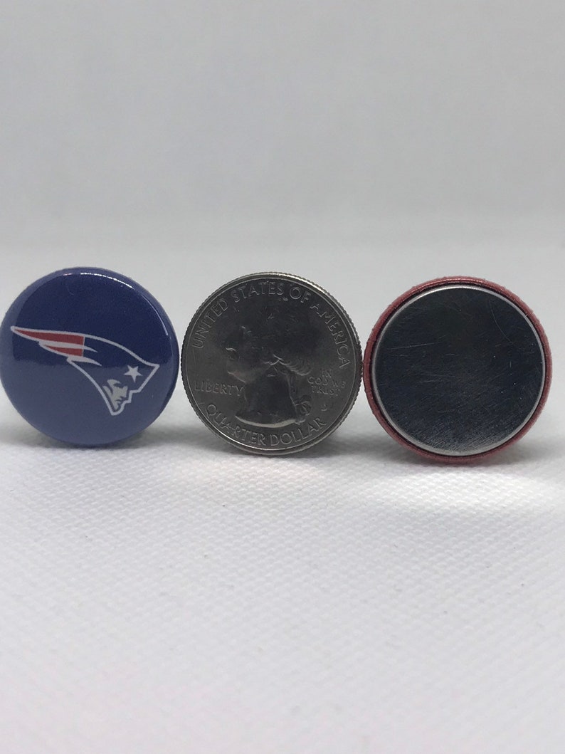 May include: Three round buttons, one with a blue background and a white and red logo of a football team, one with a silver US quarter with the text "UNITED STATES OF AMERICA" and "LIBERTY" and "QUARTER DOLLAR", and one with a red and silver button.